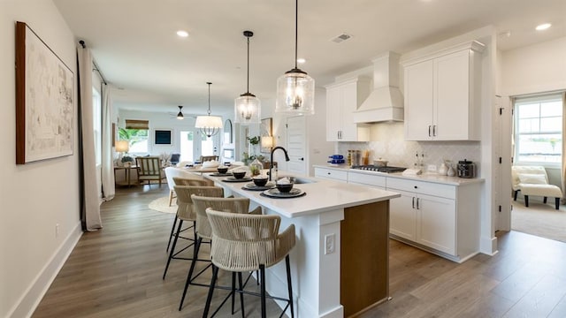 kitchen featuring premium range hood, a sink, wood finished floors, stainless steel gas cooktop, and a center island with sink