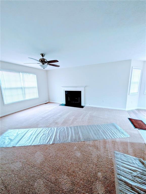 unfurnished living room with a fireplace with flush hearth, a healthy amount of sunlight, and carpet flooring