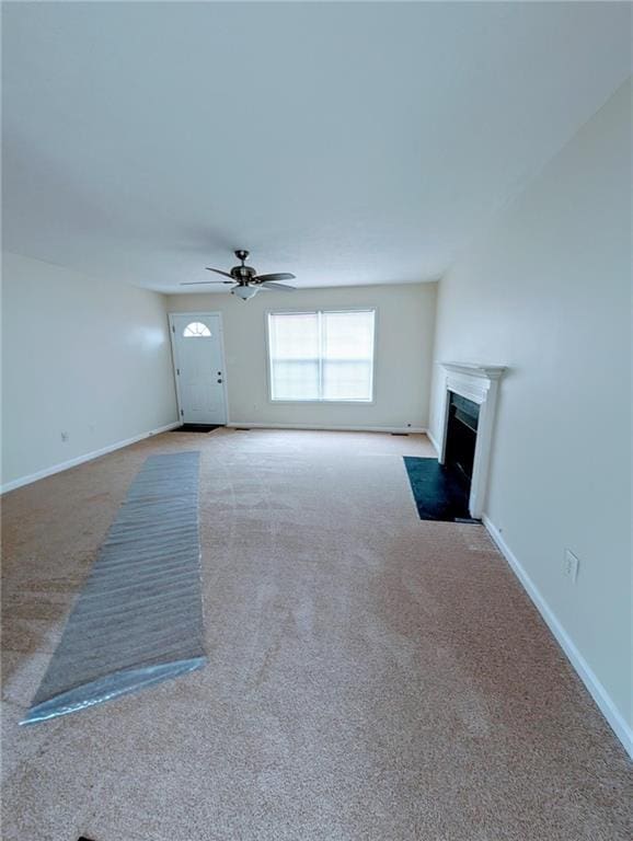 unfurnished living room with carpet floors, baseboards, ceiling fan, and a fireplace with flush hearth