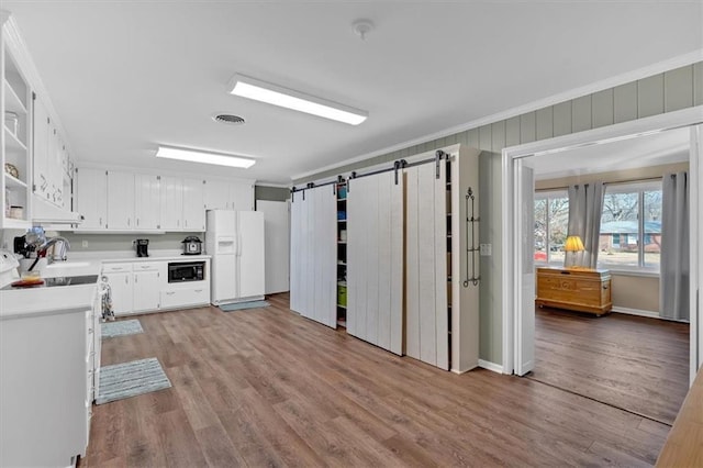 kitchen with white cabinetry, black microwave, white refrigerator with ice dispenser, light hardwood / wood-style floors, and a barn door