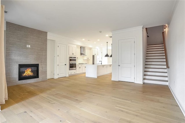 unfurnished living room featuring a tile fireplace, ornamental molding, sink, and light hardwood / wood-style floors