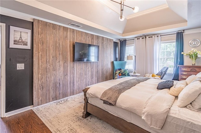 bedroom with wood walls, a chandelier, a tray ceiling, hardwood / wood-style flooring, and ornamental molding