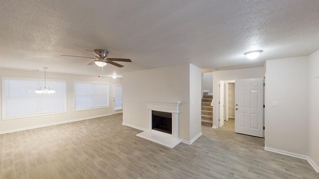 unfurnished living room with ceiling fan with notable chandelier, light hardwood / wood-style flooring, and a textured ceiling