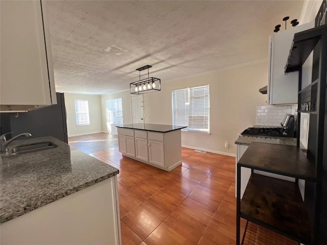 kitchen featuring white cabinets, decorative light fixtures, backsplash, sink, and dark stone countertops