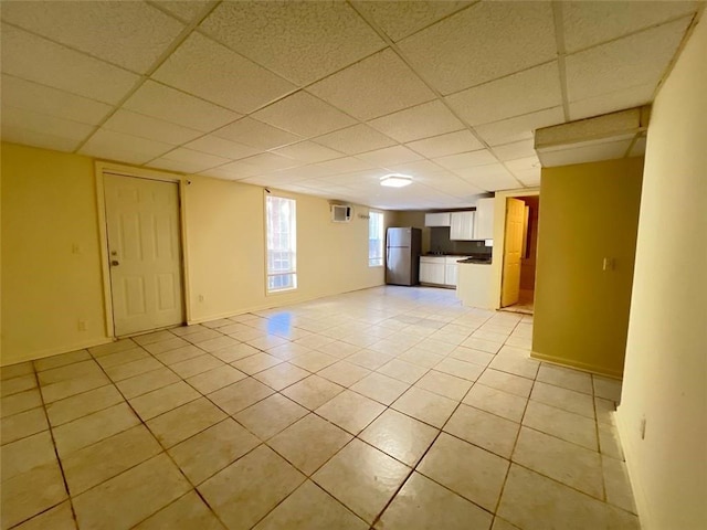 empty room with light tile patterned flooring, a wall mounted air conditioner, and a drop ceiling