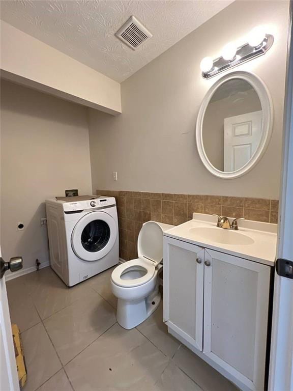 bathroom with tile walls, vanity, a textured ceiling, washer / clothes dryer, and toilet