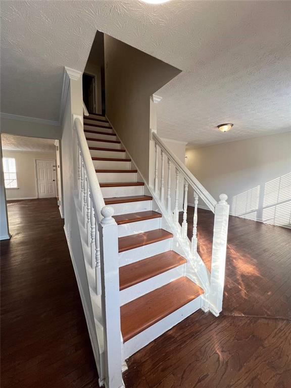 staircase featuring hardwood / wood-style floors, crown molding, and a textured ceiling