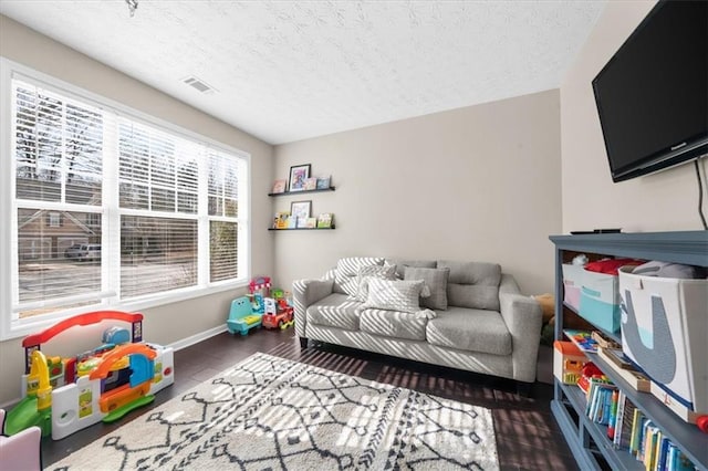 playroom featuring baseboards, visible vents, dark wood-type flooring, and a textured ceiling