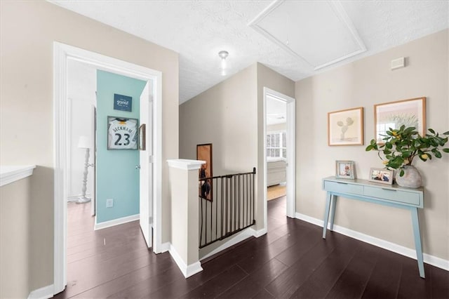 corridor featuring dark wood-type flooring, an upstairs landing, attic access, and baseboards