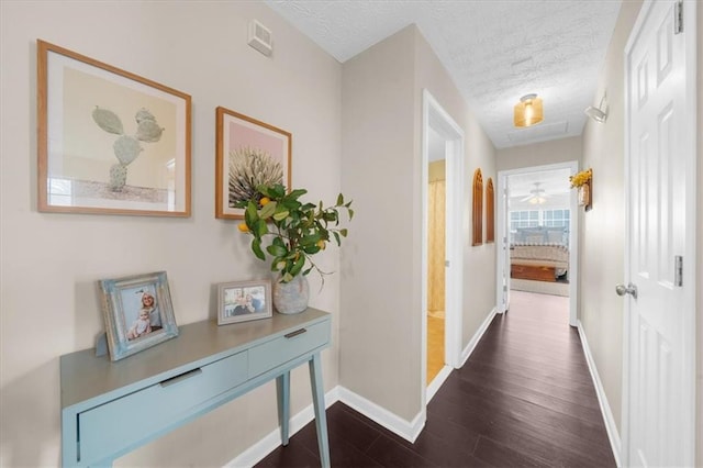 hall featuring a textured ceiling, dark wood-style flooring, and baseboards