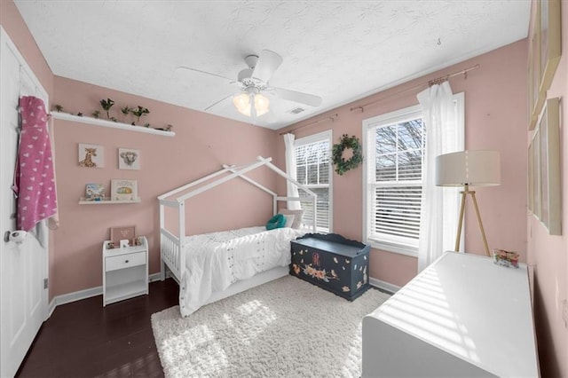 bedroom with a ceiling fan, a textured ceiling, baseboards, and dark wood-type flooring