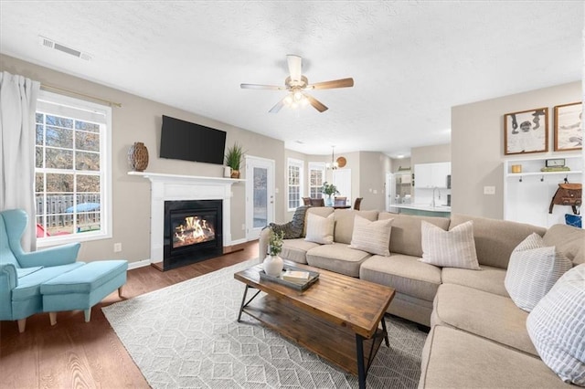 living room with a glass covered fireplace, wood finished floors, visible vents, and a healthy amount of sunlight