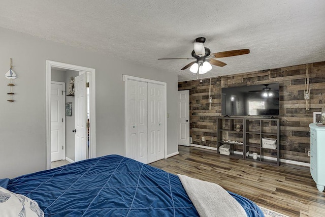 4434 Hidden Oaks Dr, Flowery Branch, GA 30542 - bedroom with a textured ceiling, wood finished floors, wood walls, a closet, and ceiling fan