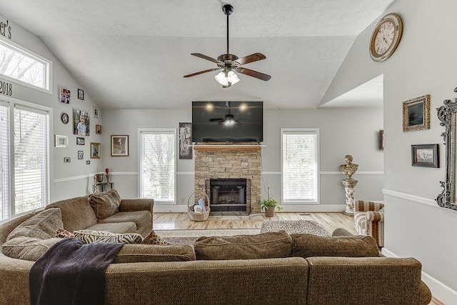 4434 Hidden Oaks Dr, Flowery Branch, GA 30542 - living room with a textured ceiling, wood finished floors, ceiling fan, a stone fireplace, and healthy amount of natural light