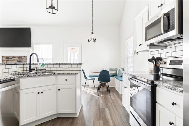 kitchen with white cabinetry, appliances with stainless steel finishes, light stone counters, and decorative light fixtures