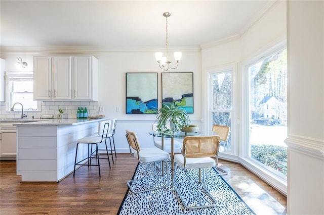 dining area with dark wood-type flooring, ornamental molding, an inviting chandelier, and sink