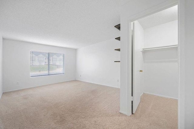 unfurnished bedroom featuring a walk in closet, a textured ceiling, a closet, baseboards, and light colored carpet