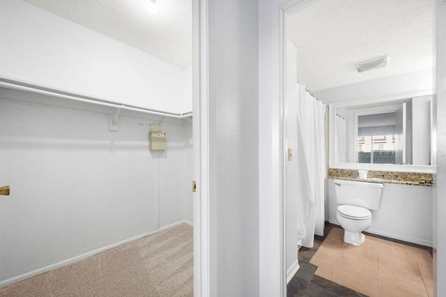 bathroom featuring curtained shower, a textured ceiling, toilet, and a walk in closet