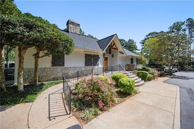 view of front of house featuring stone siding, a chimney, stairs, and a shingled roof