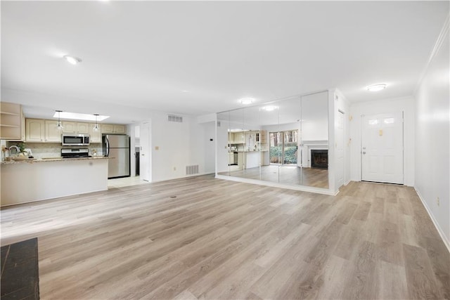 unfurnished living room with light wood finished floors, visible vents, crown molding, baseboards, and a fireplace