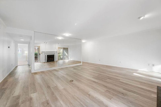 unfurnished living room with a fireplace with raised hearth and light wood-type flooring