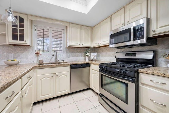 kitchen featuring a sink, tasteful backsplash, appliances with stainless steel finishes, light tile patterned floors, and glass insert cabinets