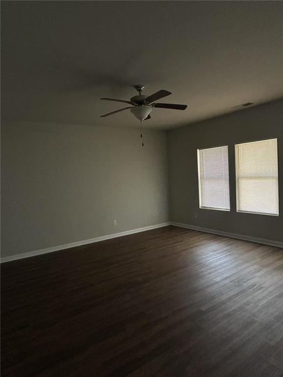 unfurnished room with ceiling fan, visible vents, baseboards, and dark wood-type flooring