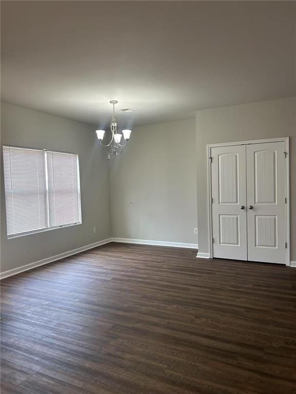 spare room with dark wood-type flooring, a chandelier, and baseboards