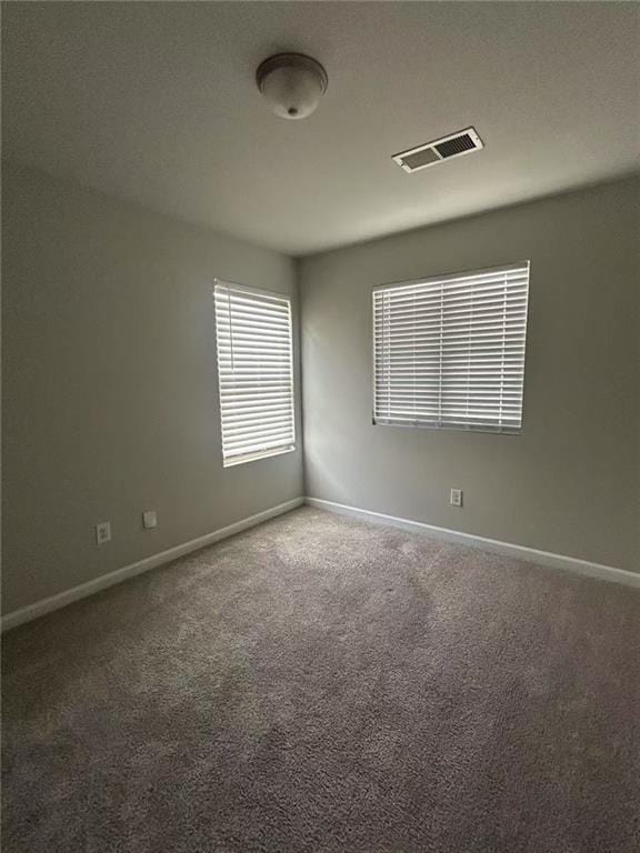 spare room with carpet flooring, visible vents, and baseboards