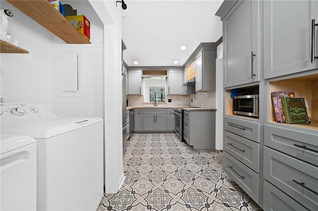 kitchen featuring gray cabinetry, stainless steel appliances, tasteful backsplash, washer and dryer, and a sink