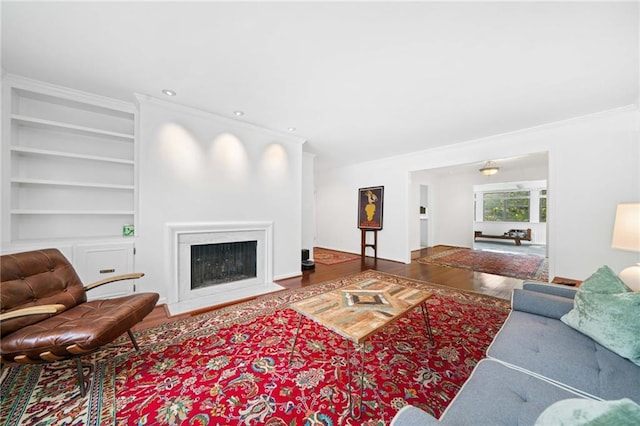 living area featuring wood finished floors, built in features, crown molding, a fireplace, and recessed lighting