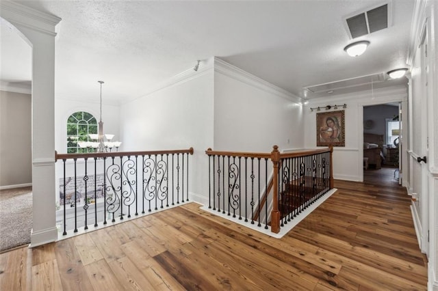 corridor with hardwood / wood-style floors, a textured ceiling, crown molding, and a chandelier