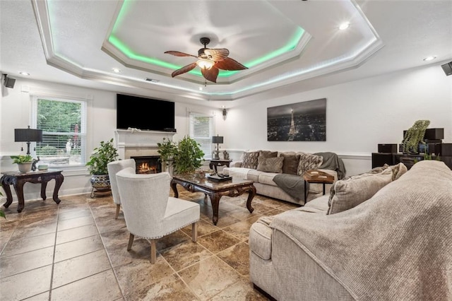 living room featuring a raised ceiling, ceiling fan, and crown molding