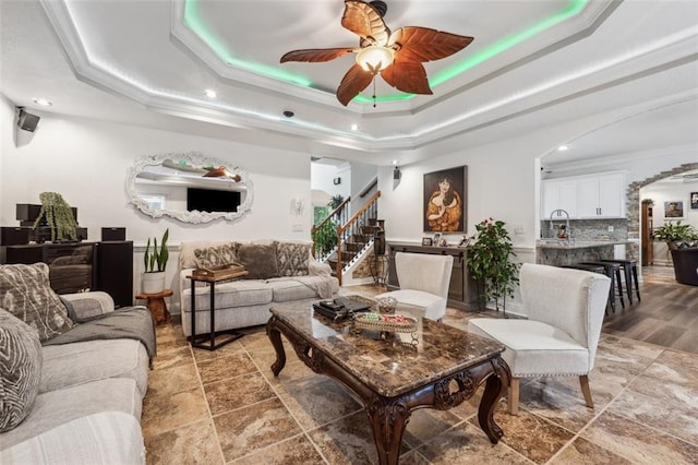 living room with ceiling fan, a raised ceiling, ornamental molding, and sink