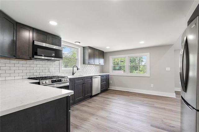 kitchen featuring tasteful backsplash, a sink, stainless steel appliances, baseboards, and light wood-type flooring