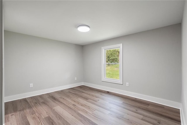 spare room featuring wood finished floors, visible vents, and baseboards