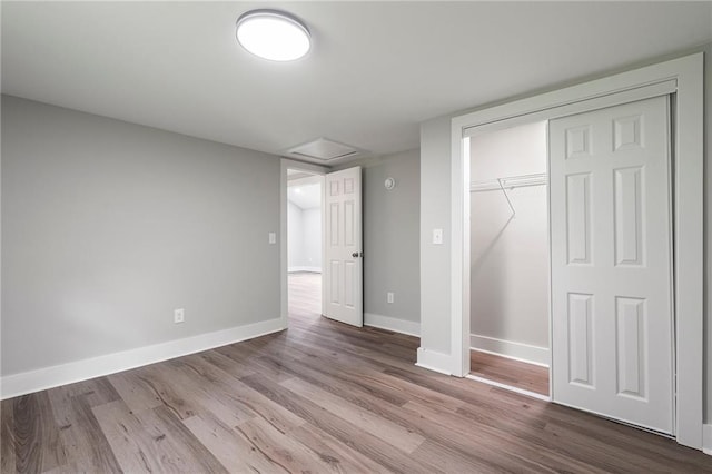 unfurnished bedroom featuring baseboards, attic access, wood finished floors, and a closet