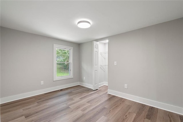 empty room with wood finished floors, visible vents, and baseboards
