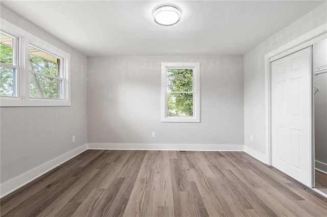 unfurnished bedroom with multiple windows, baseboards, wood finished floors, and visible vents