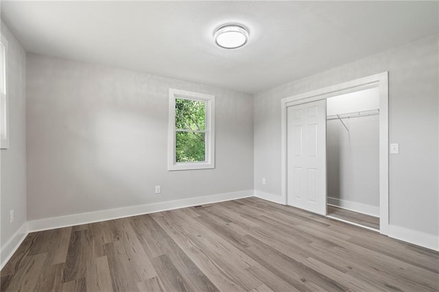 unfurnished bedroom featuring wood finished floors, baseboards, and a closet