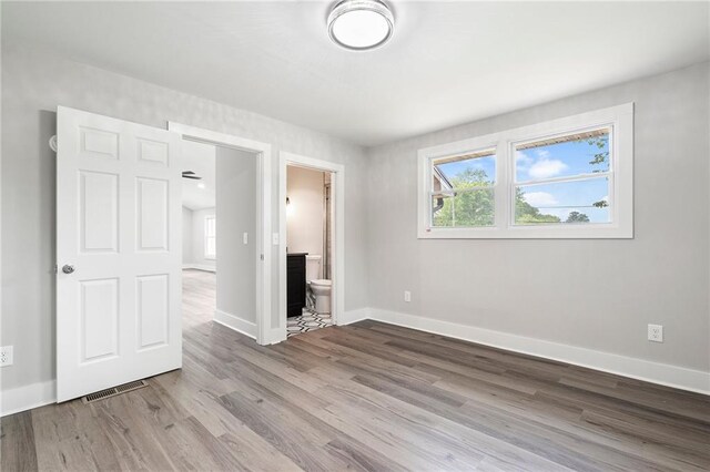unfurnished bedroom with baseboards, visible vents, wood finished floors, and ensuite bath