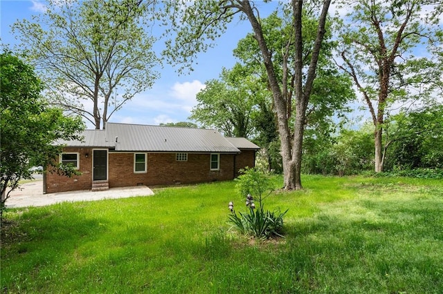 back of property featuring metal roof, brick siding, a yard, and a patio area