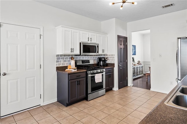 kitchen with visible vents, stainless steel appliances, dark countertops, tasteful backsplash, and a sink
