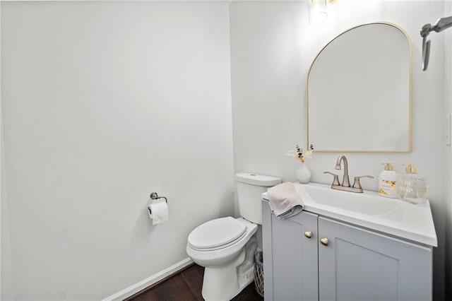 half bathroom featuring baseboards, wood finished floors, toilet, and vanity