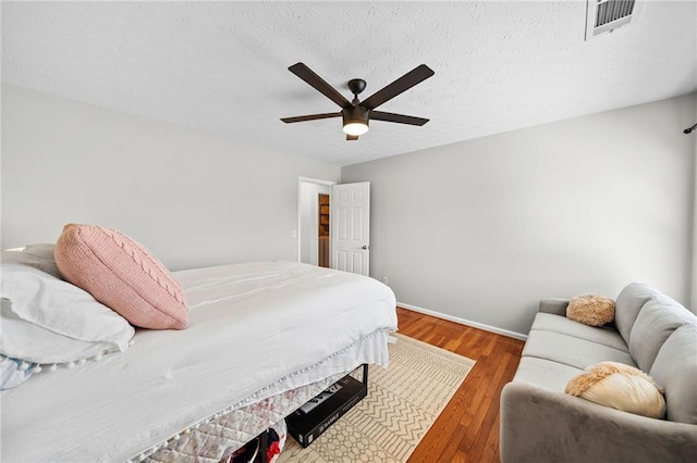 bedroom featuring a ceiling fan, wood finished floors, a textured ceiling, baseboards, and visible vents