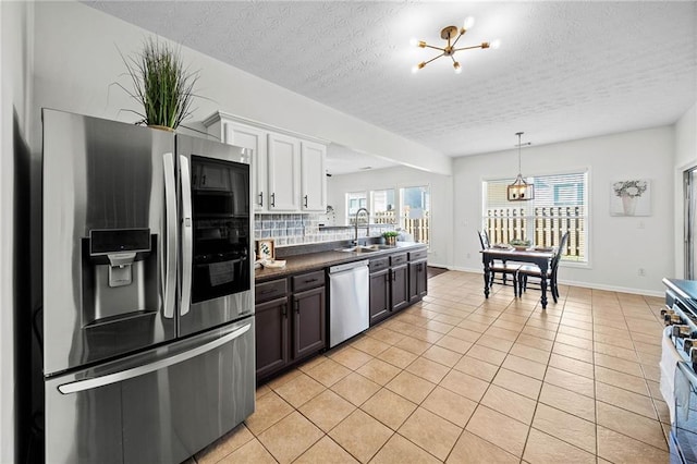 kitchen with dark countertops, tasteful backsplash, appliances with stainless steel finishes, a sink, and an inviting chandelier