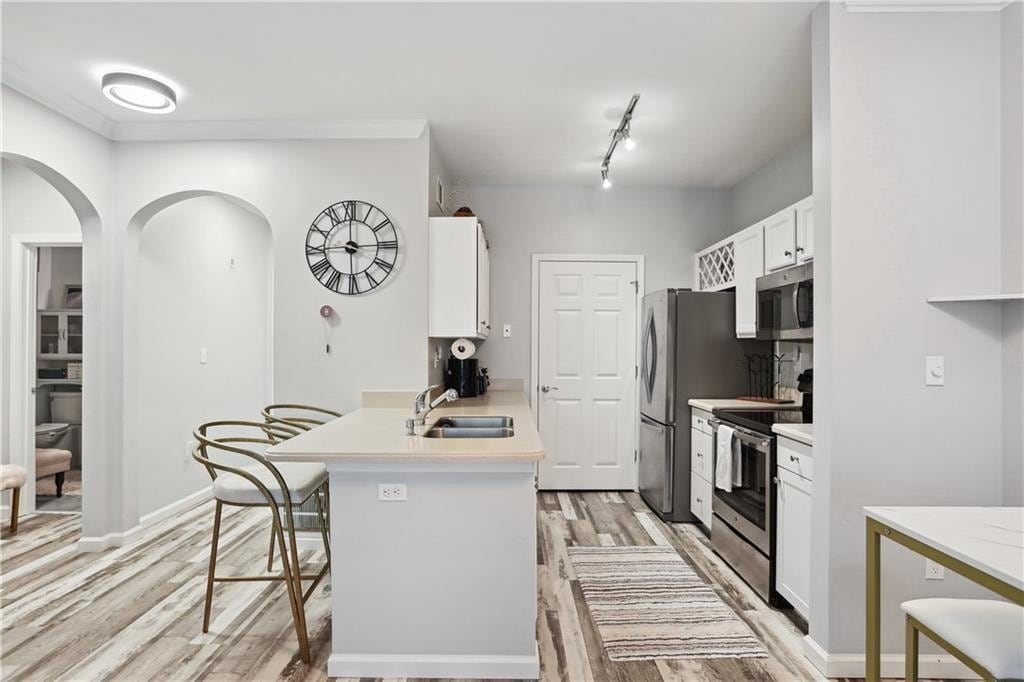 kitchen featuring a breakfast bar, a sink, white cabinetry, light countertops, and appliances with stainless steel finishes