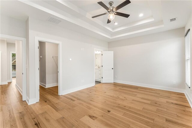 empty room with light hardwood / wood-style floors, a raised ceiling, and ceiling fan