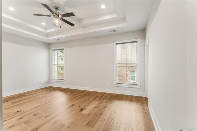 spare room with ceiling fan, a tray ceiling, plenty of natural light, and light wood-type flooring