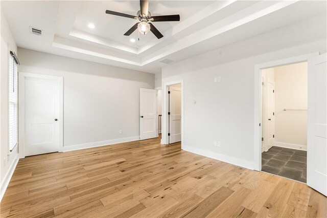 unfurnished bedroom with a raised ceiling, hardwood / wood-style flooring, and ceiling fan